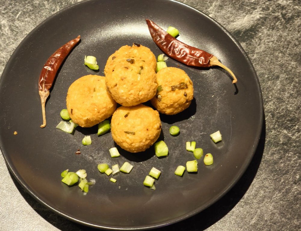 Gato Pima, frittierte Spalterbsen-Bällchen mit Frühlingszwiebeln und getrockneten Chilis auf einem dunklen Teller