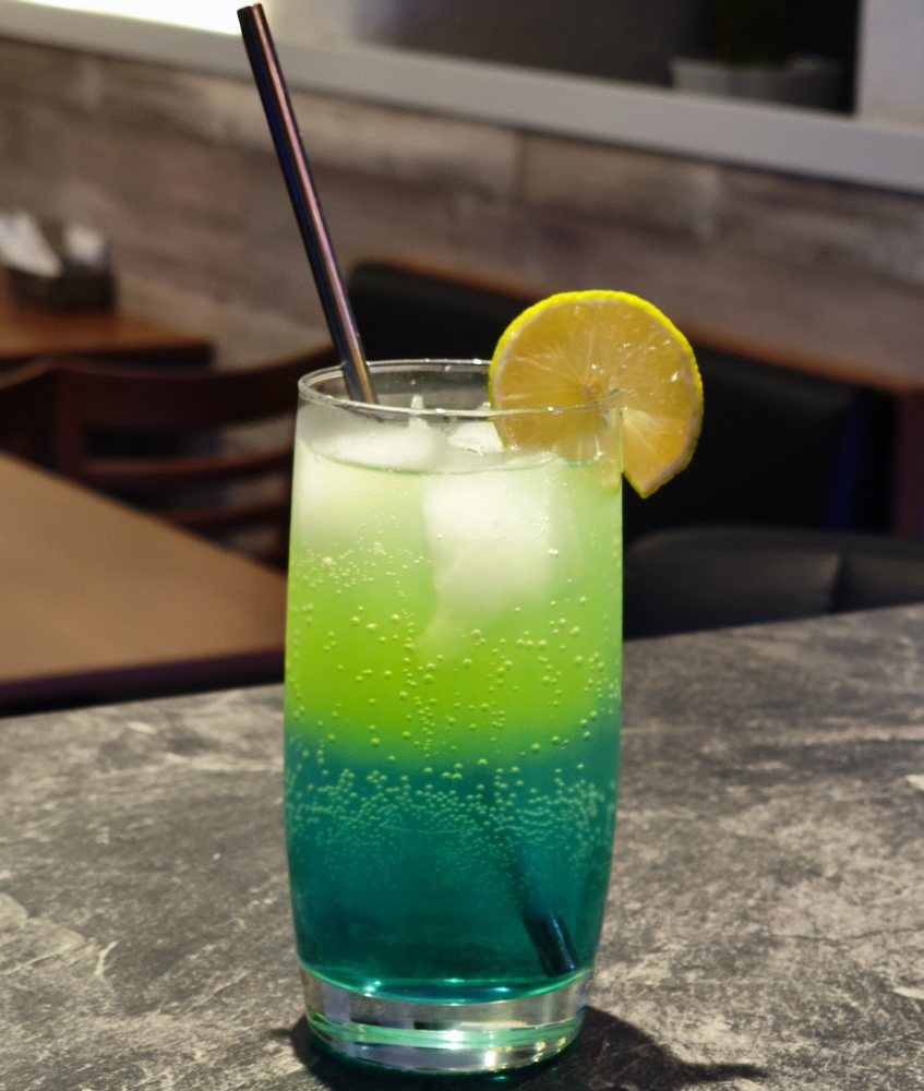 Grün-blaues Erfrischungsgetränk mit Limettenscheibe und Metallstrohhalm