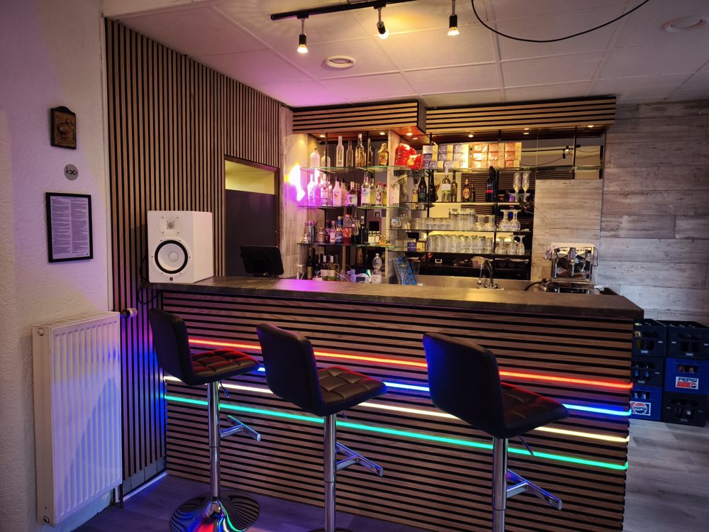 Bar im Restaurant mit Holzlamellen, Barhockern und bunter LED-Beleuchtung